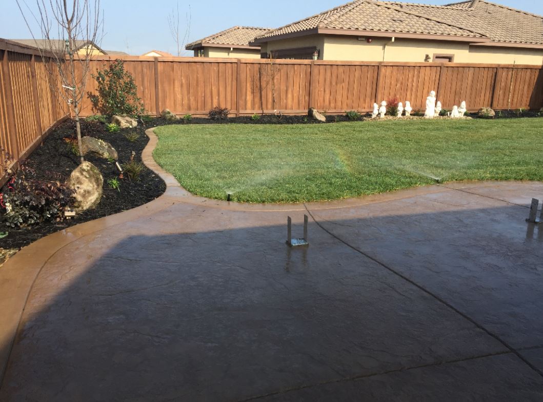 a stamped concrete patio that was cleverly cut and the sprinklers in the backyard are running. This masonry contractor is enthused as is the customer