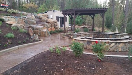a picture of a backyard full of stamped concrete, stone seating areas, concrete stairs, and natural stone boulders near a patio cover done by the best Rocklin concrete and masonry contractor in the biz